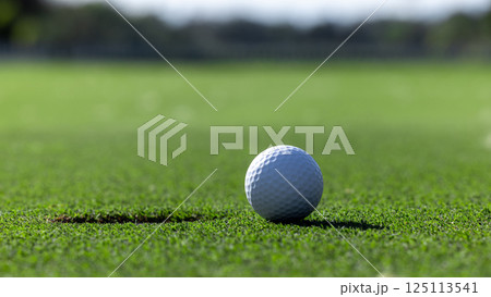 In the hole, White golf ball on green grass with golf hole, Golf ball ready to be shot, Golf ball close up on green grass in the hole, Top view. 125113541