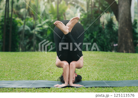 Asian woman practicing yoga in Supported Headstand Pose on the mat in outdoor park. Asian woman practicing yoga in Supported Headstand Pose on the mat in outdoor park. 125113576