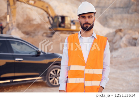 Posing for a camera. Man in uniform is working in the quarry at daytime Posing for a camera. Man in uniform is working in the quarry at daytime 125113614