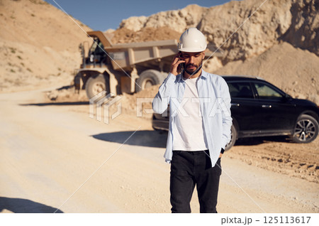 Business conversation by phone. Man in uniform is working in the quarry at daytime Business conversation by phone. Man in uniform is working in the quarry at daytime 125113617