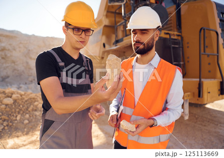 Checking rock that is in the hands. Two men in uniform are working together in the quarry Checking rock that is in the hands. Two men in uniform are working together in the quarry 125113669
