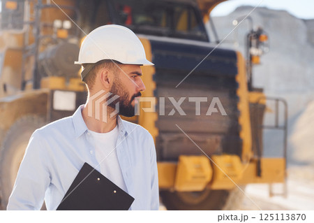 Big haul track behind. Man in uniform is working in the quarry at daytime Big haul track behind. Man in uniform is working in the quarry at daytime 125113870