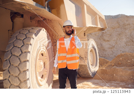 Using smartphone. Man in uniform is working in the quarry at daytime 125113943