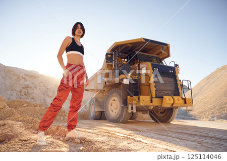 Young woman in red pants and black top is standing in the quarry against haul truck Young woman in red pants and black top is standing in the quarry against haul truck 125114046