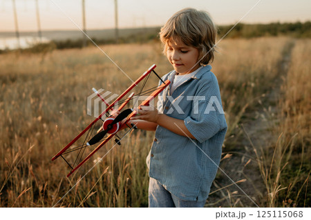 Smiling preschool child boy plays with craft wooden retro styled airplane Smiling preschool child boy plays with craft wooden retro styled airplane 125115068