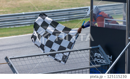 Man holding and waving checkered race flag on finish podium, Finish line and checkered flag, Race flag at the finish line on a race track, Victory achievement success motorsport. Man holding and waving checkered race flag on finish podium, Finish line and checkered flag, Race flag at the finish line on a race track, Victory achievement success motorsport. 125115230