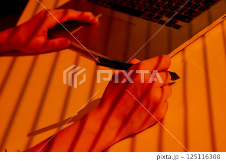Woman Using Stylus to Draw Beside Laptop in Warm Office Light. 125116308