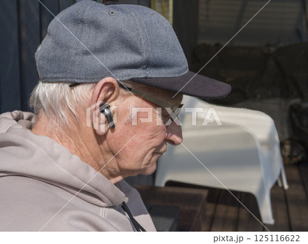 Mature male with baseball cap and hoodie listening to music through wireless earbuds, leaning against rustic wooden surface, immersed in private audio world Mature male with baseball cap and hoodie listening to music through wireless earbuds, leaning against rustic wooden surface, immersed in private audio world 125116622