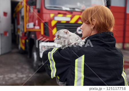 View from behind. Holding cat on shoulders. Woman firefighter in uniform is at work in department View from behind. Holding cat on shoulders. Woman firefighter in uniform is at work in department 125117758