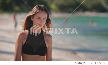 Young woman joyfully strolls along a white sandy beach with crystal clear turquoise waters, enjoying the sunny day and carefree lifestyle of a tropical paradise 125117797