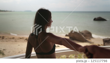 Woman in bikini stand on hotel villa balcony hold boyfriend hand show beautiful sea view sand beach ocean landscape. Travel Thailand exotic island. Couple tourist on summer vacation. Lifestyle holiday Woman in bikini stand on hotel villa balcony hold boyfriend hand show beautiful sea view sand beach ocean landscape. Travel Thailand exotic island. Couple tourist on summer vacation. Lifestyle holiday 125117798