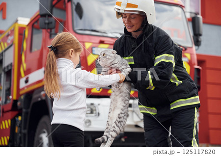 Near the truck. With scottish fold cat. Firefighter woman in uniform is with a little girl 125117820