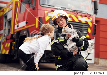 Near the truck. With scottish fold cat. Firefighter woman in uniform is with a little girl Near the truck. With scottish fold cat. Firefighter woman in uniform is with a little girl 125117821