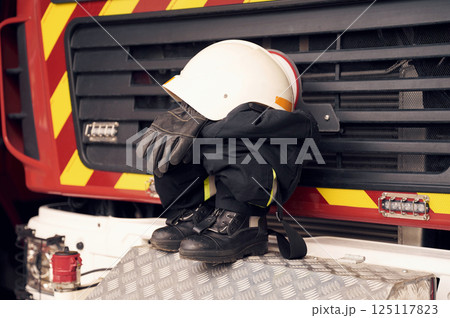 Close up view of firefighter's hat, gloves, jacket, pants and shoes. With big vehicle Close up view of firefighter's hat, gloves, jacket, pants and shoes. With big vehicle 125117823