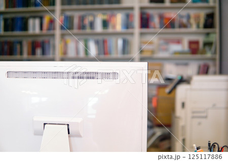 Close-up of a white computer monitor in a library with bookshelf in the background 125117886