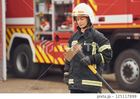 Standing with axe in hands against truck. Woman firefighter in uniform is at work in department Standing with axe in hands against truck. Woman firefighter in uniform is at work in department 125117899
