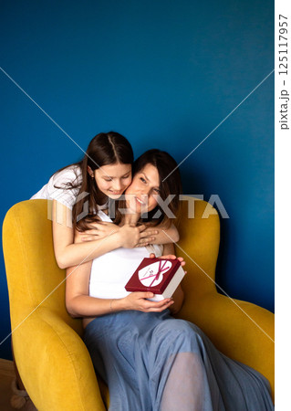 Happy mother's day. Preteen daughter hugs and congratulates moms giving her gift box. Motherhood concept. 125117957