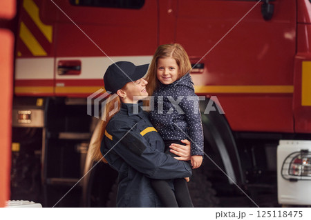 Firefighter woman in uniform is holding a little girl in the hands Firefighter woman in uniform is holding a little girl in the hands 125118475