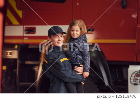 Firefighter woman in uniform is holding a little girl in the hands Firefighter woman in uniform is holding a little girl in the hands 125118476