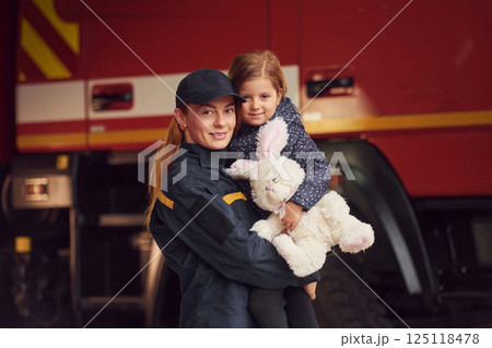Against big truck. With bunny toy. Firefighter woman in uniform is with a little girl 125118478