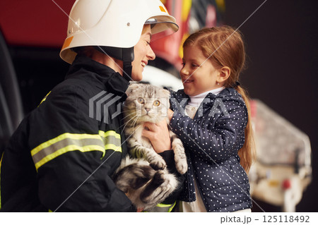 Giving beautiful scottish fold cat. Firefighter woman in uniform is with a little girl Giving beautiful scottish fold cat. Firefighter woman in uniform is with a little girl 125118492