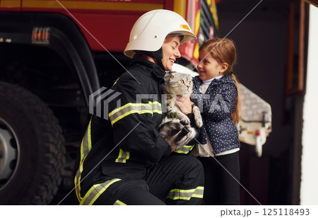 Giving beautiful scottish fold cat. Firefighter woman in uniform is with a little girl Giving beautiful scottish fold cat. Firefighter woman in uniform is with a little girl 125118493