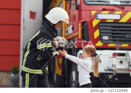 Giving beautiful scottish fold cat. Firefighter woman in uniform is with a little girl Giving beautiful scottish fold cat. Firefighter woman in uniform is with a little girl 125118496