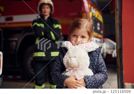 Kid is holding bunny toy. Firefighter woman in uniform is with a little girl 125118509