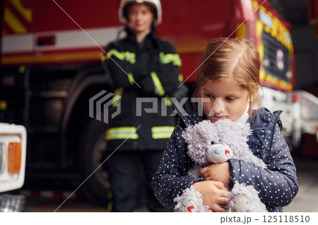 Kid is holding bunny toy. Firefighter woman in uniform is with a little girl 125118510