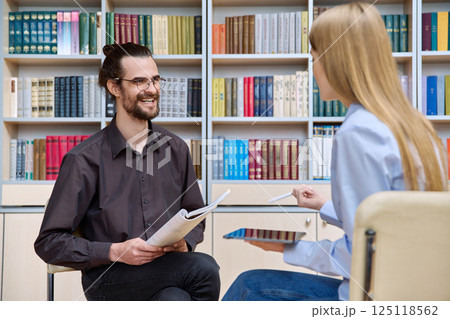 Young male psychologist, college worker counseling teenage student girl in library, office 125118562