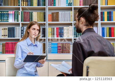 Teenage student girl talking with male teacher, social worker, school counselor in library Teenage student girl talking with male teacher, social worker, school counselor in library 125118563