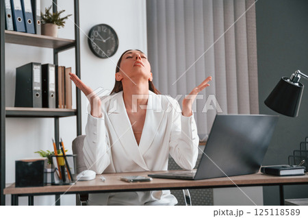 Sitting, smiling and raising hands. Young beautiful woman in formal clothes is working at office 125118589