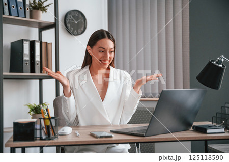 Sitting, smiling and raising hands. Young beautiful woman in formal clothes is working at office 125118590