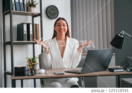 Sitting, smiling and raising hands. Young beautiful woman in formal clothes is working at office 125118591