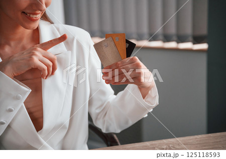 Sitting and holding three credit cards. Young beautiful woman in formal clothes is working at office 125118593