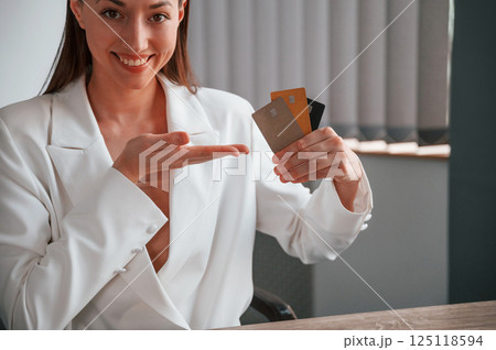 Sitting and holding three credit cards. Young beautiful woman in formal clothes is working at office 125118594