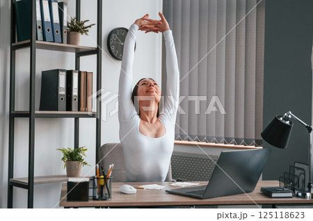 Takes a break, stretches her hands. Young beautiful woman in white clothes is in the office Takes a break, stretches her hands. Young beautiful woman in white clothes is in the office 125118623