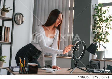 Setting up the smartphone for recording. Young beautiful woman in white clothes is in the office Setting up the smartphone for recording. Young beautiful woman in white clothes is in the office 125118671
