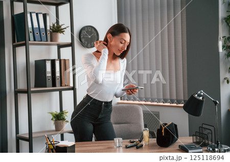 Standing and using laptop. Young beautiful woman in white clothes is in the office 125118694