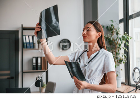 Holding x-ray of bones. Young beautiful female doctor in white coat is in the office 125118719