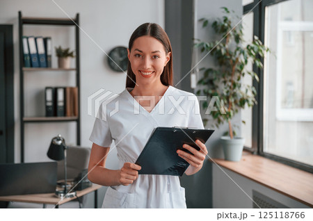 Smiling young beautiful woman in white clothes is in the office with notepad Smiling young beautiful woman in white clothes is in the office with notepad 125118766