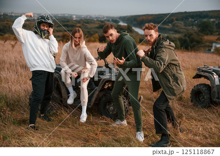 Two couples is with quad bikes on the field. Men are having fun and showing the fists Two couples is with quad bikes on the field. Men are having fun and showing the fists 125118867