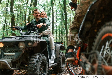 Lovely couple is sitting on the ATV with man on motorcycle in the forest Lovely couple is sitting on the ATV with man on motorcycle in the forest 125118892