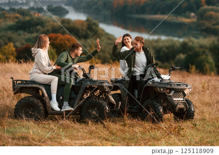 Giving high five and smiling. Two young couples with quad bikes is together on the field Giving high five and smiling. Two young couples with quad bikes is together on the field 125118909