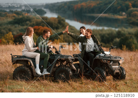 Giving high five and smiling. Two young couples with quad bikes is together on the field 125118910