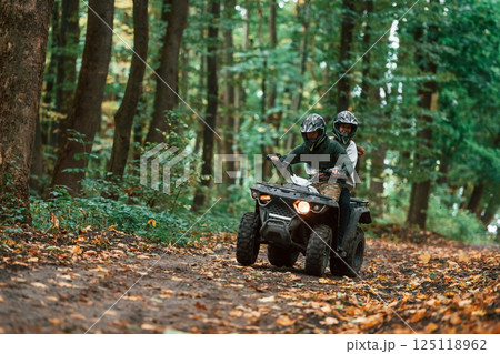 Driving on the footpath. Young couple riding a quad bike in the forest Driving on the footpath. Young couple riding a quad bike in the forest 125118962