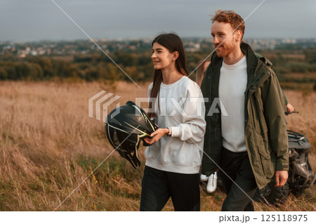 Walking and smiling. Lovely young couple is with quad bike outdoors on the field Walking and smiling. Lovely young couple is with quad bike outdoors on the field 125118975
