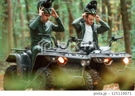 Wearing helmets. Two male atv riders is in the forest together Wearing helmets. Two male atv riders is in the forest together 125119071