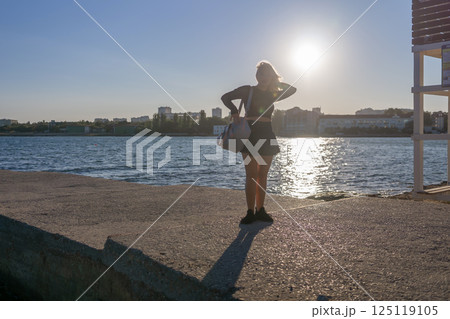 Woman, Sunset, Waterfront - Silhouette of woman standing on waterfront with sunset in background. 125119105