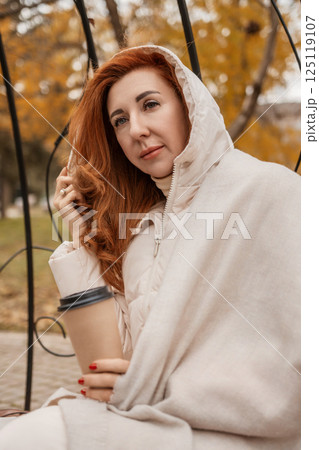 Woman Autumn Park Portrait: Redhead pensive pose, beige shawl, fall foliage backdrop. Woman Autumn Park Portrait: Redhead pensive pose, beige shawl, fall foliage backdrop. 125119107